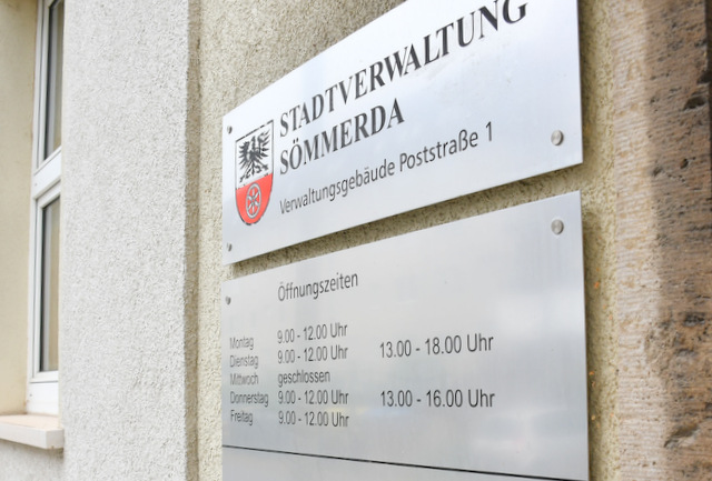Eine Edelstahltafel mit Aufschrift Verwaltungsgebäude Poststraße und den Öffnungszeiten hängt am Gebäude.